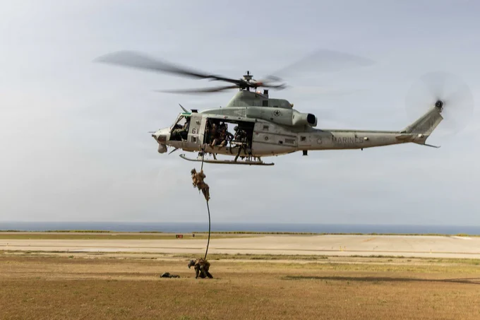 A U.S. Marine fast-ropes from a UH-1Y Venom helicopter during an aviation assault training exercise over a coastal landing zone.