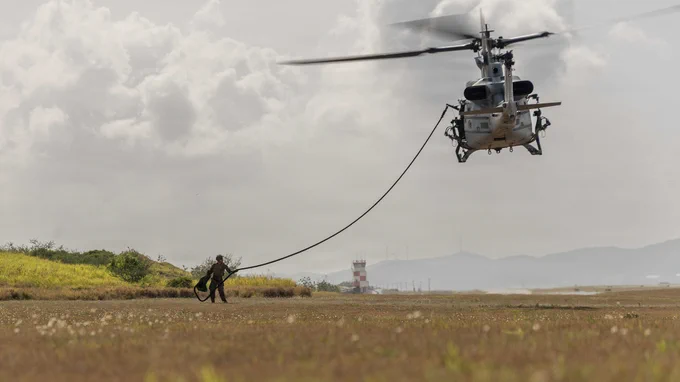 A U.S. Marine gathers a fast rope after helicopter insertion training as a UH-1Y Venom departs overhead.