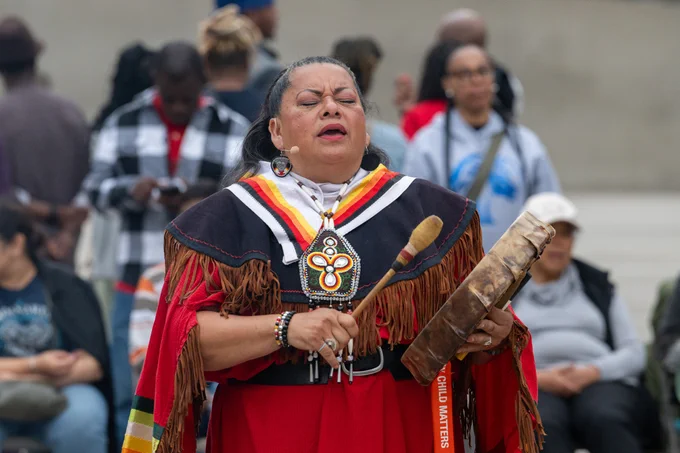 An Indigenous person in traditional regalia holding a drum and beater during last year's ceremony.