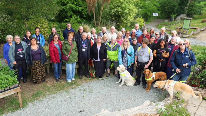 A group of volunteers, staff and guide dogs standing outside at Fairhaven Woodland and Water Garden.