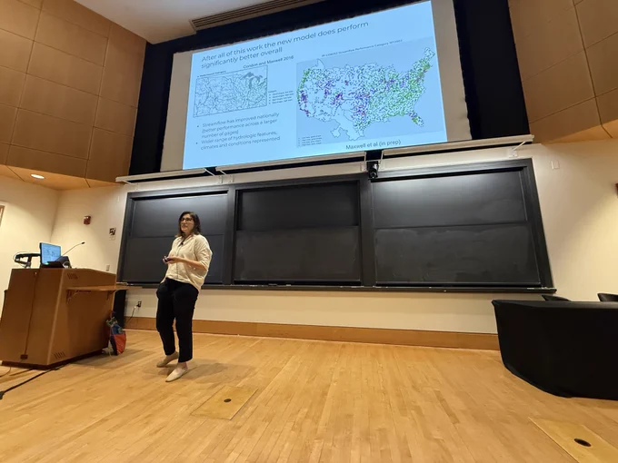 Laura Condon presents her featured talk in a lecture hall, with a streamflow performance map displayed on the slide behind her.