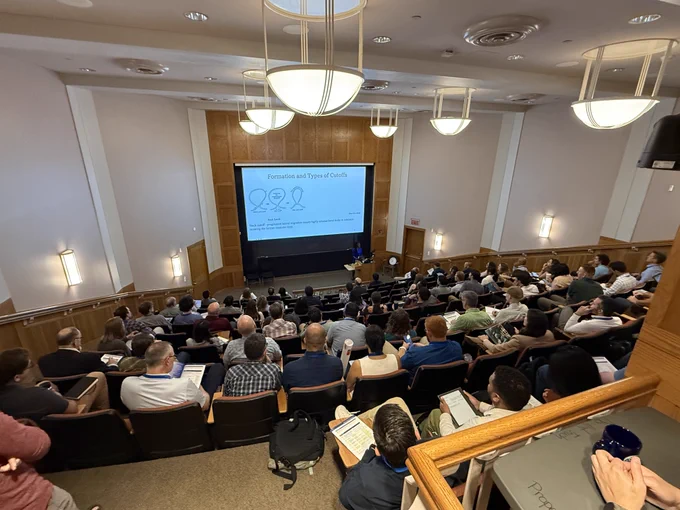A presenter stands at the front of a packed lecture hall delivering her talk, with a slide behind her titled "Formation and Types of Cutoffs."