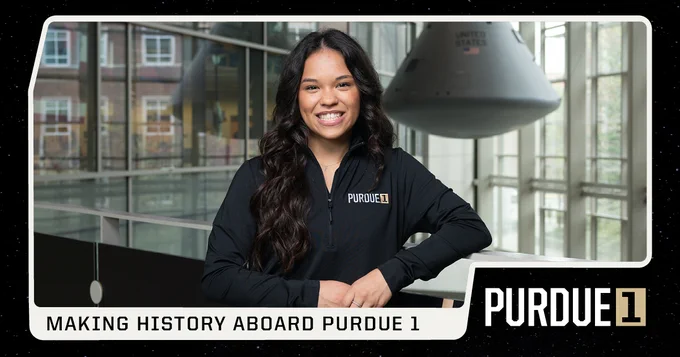 Abigail wearing a "PURDUE 1" jacket is smiling and standing indoors with a space capsule in the background. The text reads, "Making History Aboard Purdue 1.