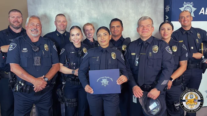 Group of police officers in uniform posing together, one holding a certificate with a police badge emblem.