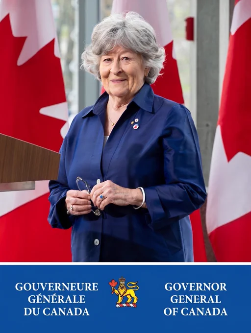 Official portrait of the Governor General of Canada, an older woman with wavy grey hair, smiling directly at the camera while wearing a dark blue silk jacket. She is holding a pair of glasses in her hands. Red and white Canadian flags are visible in the background. At the bottom, a navy blue banner features the Canadian crest alongside institutional text in French and English: "Gouverneure générale du Canada" and "Governor General of Canada".