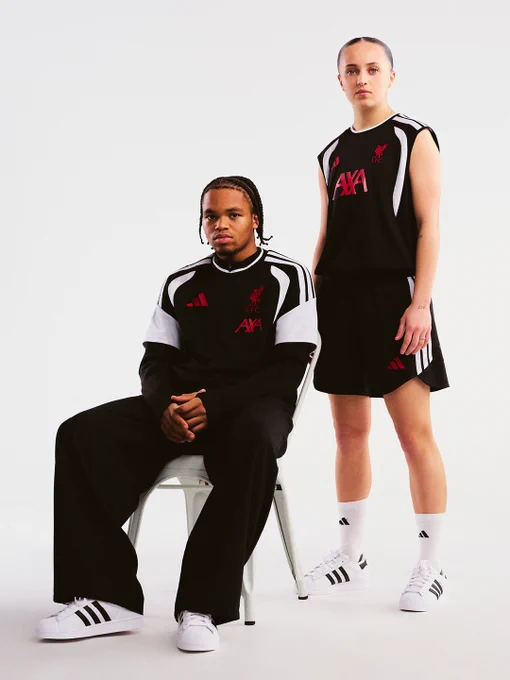 Rio Engumoha and Mia Enderby in Liverpool FC training wear against a white background, one seated in a black long-sleeve top and track pants with white adidas trainers, the other standing in a black sleeveless top and skirt with white trainers.