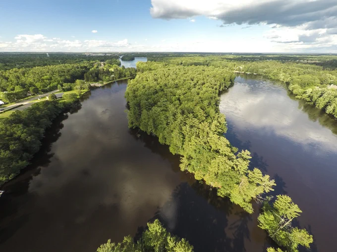 Aerial view of a winding river surrounded by dense green forest under a partly cloudy sky.