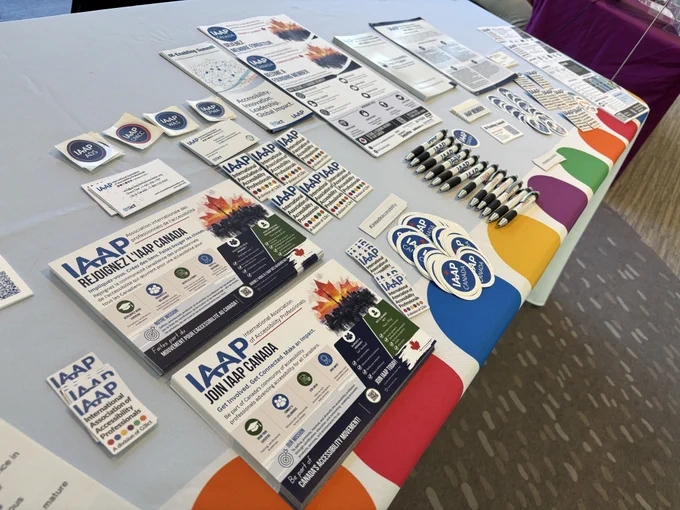 IAAP Canada Chapter booth with an IAAP Canada banner on a table that includes swag (stickers, magnets, pamphlets, papers, certification badges, etc.).