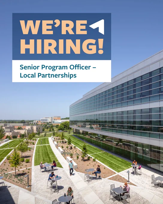 A modern office building with large glass windows is depicted. In the foreground, people sit and converse at outdoor tables on a lawn with landscaped walkways. A top left corner of the image reads, "We're Hiring! Senior Program Officer – Local Partnerships."
