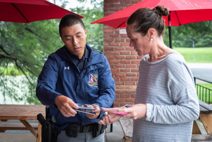 Howard County Police Department community outreach officer speaking with a member of the public and showing them a brochure during one of the department's monthly Coffee with a Cop events.