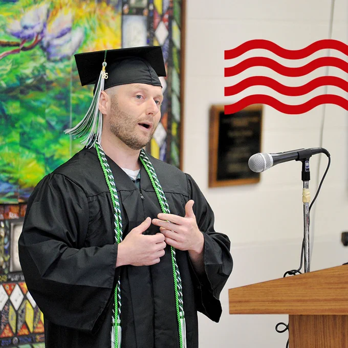 A recent graduate of the Prison Education Initiative speaks during a graduation ceremony wearing a graduation cap and gown.