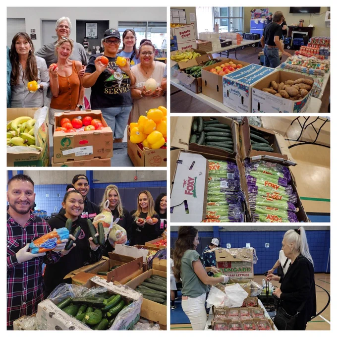 Image showing a group of people smiling and holding fresh vegetables in a community center. Tables are filled with boxes of bananas, bell peppers, potatoes, and other produce, including "Dole" and "Foxy" branded items. People are organizing and distributing food.