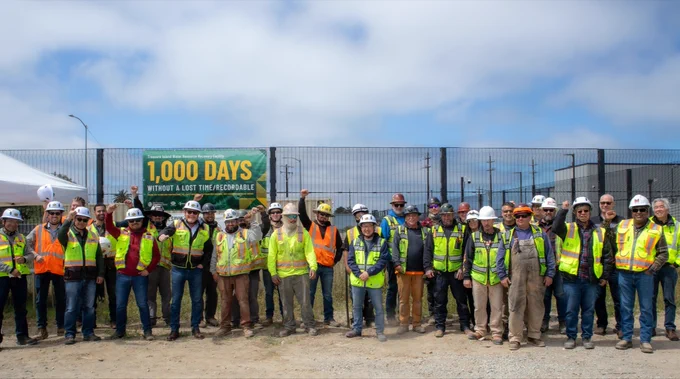 PCL Construction employees, trade partners and project stakeholders celebrate a major safety milestone at the Treasure Island Water Resource Recovery Facility in San Francisco, California. Team members raise their fists in front of a banner recognizing 1,000 days without a lost-time or recordable incident as the project continues to advance.