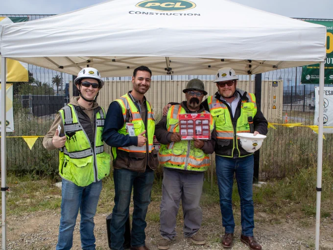 Project team members pose with a prize winner during a safety recognition event at the Treasure Island Water Resource Recovery Facility in San Francisco, California. The group stands beneath a PCL Construction tent celebrating 1,000 days without a lost-time or recordable incident.