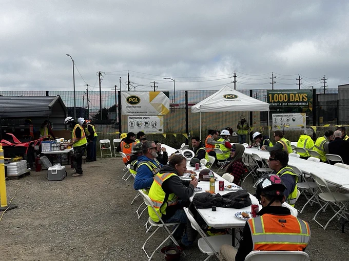 Construction professionals and trade partners gather under a PCL Construction tent at the Treasure Island Water Resource Recovery Facility in San Francisco, California, sharing a meal and celebrating the project's achievement of 1,000 days without a lost-time or recordable incident.