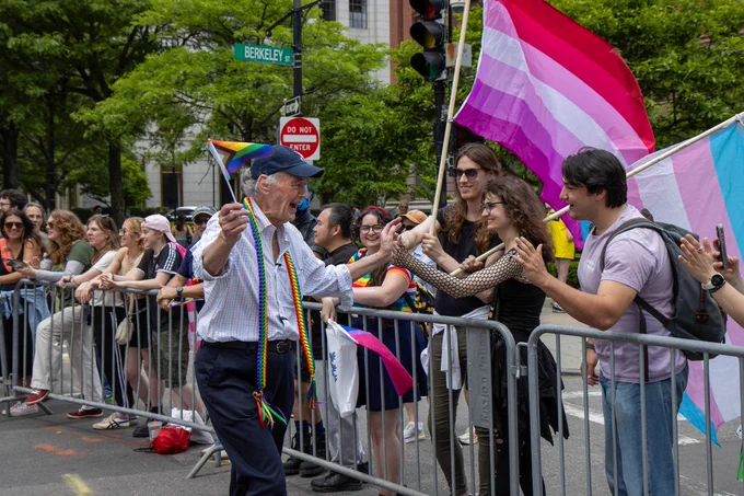 Senator Markey high fives pride attendees holding a lesbian pride flag and a trans pride flag.