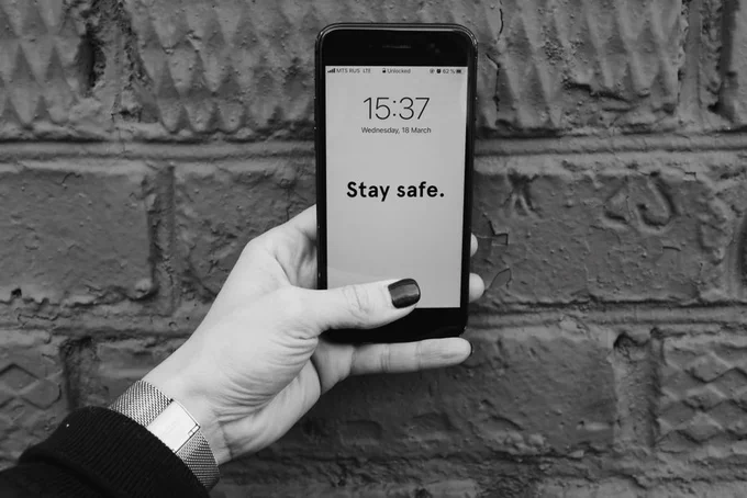 Black and white photo of a hand holding a smartphone with 'Stay safe' message.