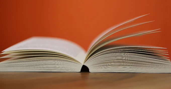 Open book on a table against a vibrant orange background.