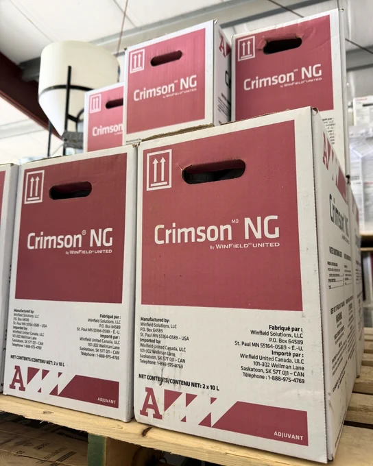 Boxes of Crimson NG by WinField United are stacked. The boxes are primarily white with red accents and include product details. They have handles for carrying.