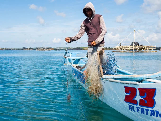 Having finally located his displaced nets, Pak Peri begins hauling the wet mesh over the wooden side of his small boat. The dripping net is heavy, but the first sections are completely empty, signalling a difficult day ahead during the July off-season.