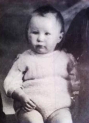 Vintage black and white photo of a baby sitting up and looking directly at the camera.
