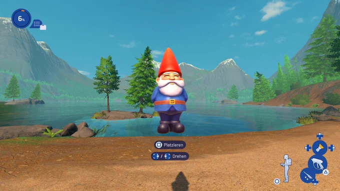 Ein riesiger Gartenzwerg mit roter Mütze und blauem Gewand steht an einem Seeufer im Spiel PowerWash Simulator 2. Im Hintergrund sind Tannen und Berge zu erkennen. Unten im Bild sieht man die Tastenbelegung zum Platzieren.