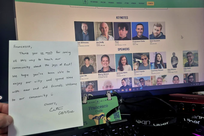A handwritten thank-you note addressed to Francesco is held in front of a monitor showing the CascadiaJS speaker lineup, with Francesco Ciulla listed among the keynote speakers. A green speaker badge with his name is clipped below the screen.
