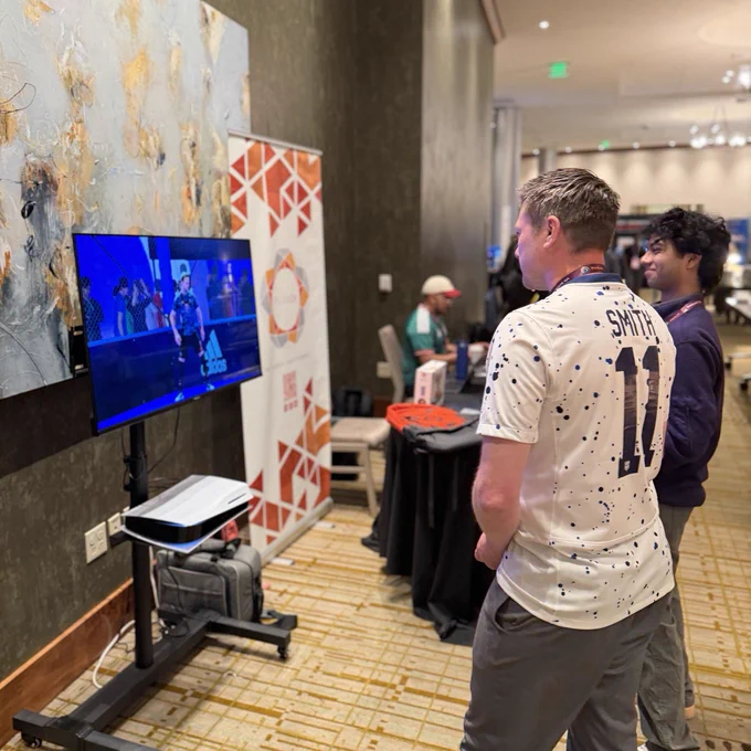 Photo of PLUS QA Team member playing video games with a conference attendee at the PLUS QA Booth. 
