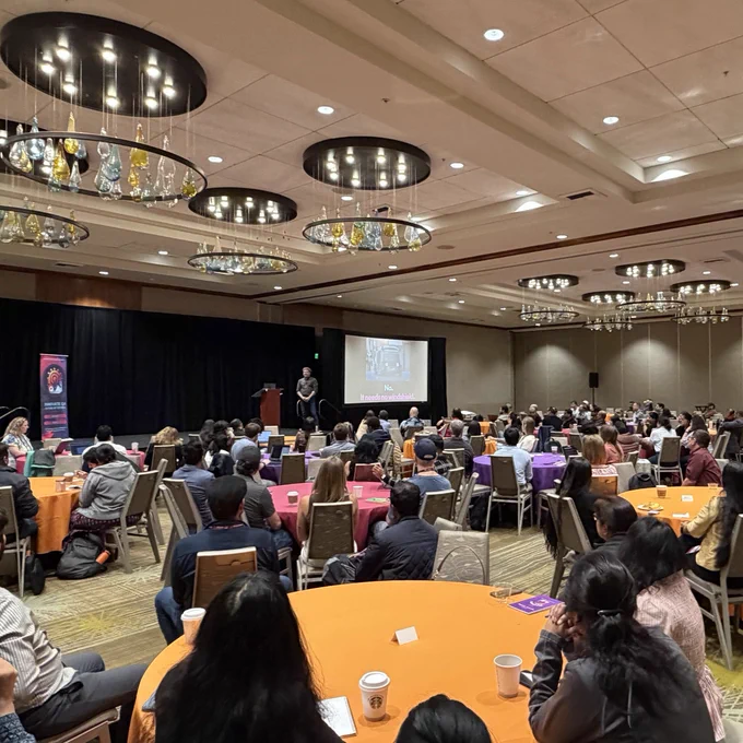 Photo of a conference room full of people looking at the stage watching the presentations. 