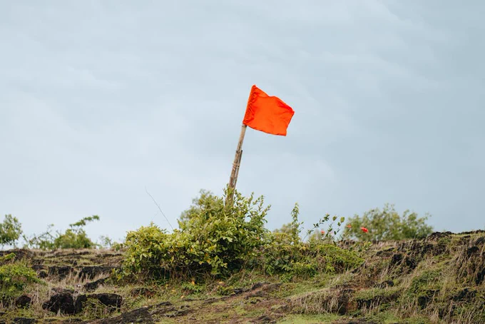 A vivid red flag waving atop a green hillside under a cloudy sky, symbolizing freedom and adventure.