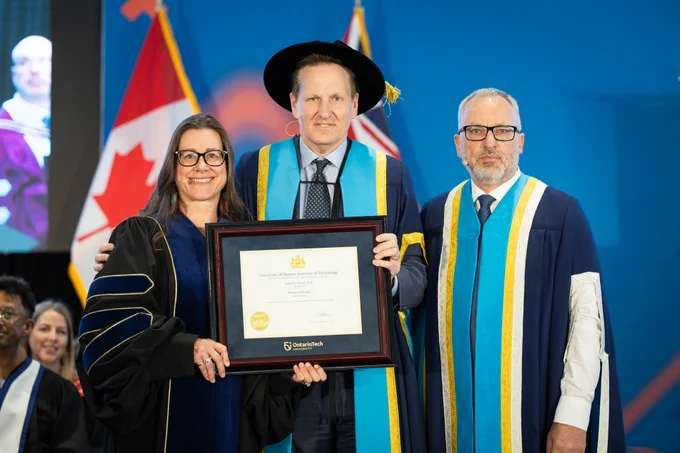 A photo of honorary degree recipient Tabatha Bull posing on stage at Ontario Tech's 2026 Spring Convocation ceremony with Ontario Tech Chancellor Mitch Frazer and Ontario Tech President Steven Murphy.

