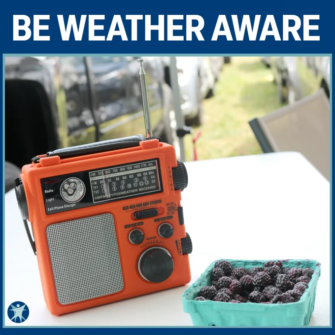 A weather radio sitting on a white plastic table at a festival campground. Be weather aware. Wisconsin Department of Health Services logo. 