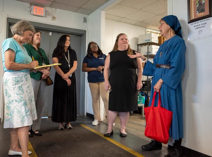 Five women, dressed in business attire, listen to a woman dressed in a nun’s habit. 
