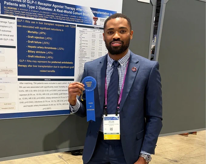 Man in a navy suit holding a blue "Poster of Distinction" ribbon beside an academic research poster.
