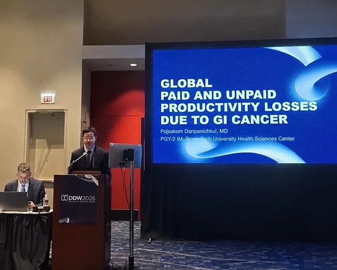 Speaker at a conference podium beside a slide titled "Global paid and unpaid productivity losses due to GI cancer."