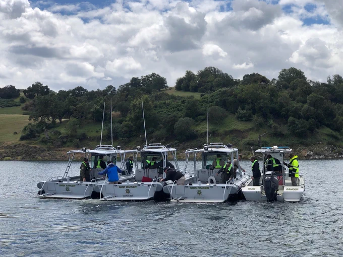 Four ranger boats with park rangers in yellow vests side by side in a reservoir.