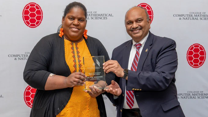 Two people holding an award in front of a CMNS step-and-repeat banner