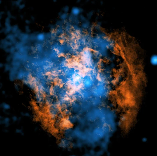 This image centers on a bright, pinpoint white glow marking Sagittarius A* (Sgr A*), the supermassive black hole at the heart of the Milky Way, surrounded by a turbulent, cloud-like environment. Radiating outward from the center is a luminous swirl of blue X-ray emission from NASA's Chandra X-ray Observatory, forming a soft, irregular halo that is brightest near the core and fades into darker shades toward the edges. Interwoven with this blue glow are thick, patchy structures in orange, tracing colder gas mapped by radio observations from ALMA. These orange regions form a partial ring and clumpy arcs around the center, but notably break open to reveal a wide, cone-shaped cavity where little to no orange emission appears. This hollowed-out region is instead filled with the blue X-ray glow, emphasizing the contrast between hot and cold material. The scene feels dynamic and layered, with the interplay of blue and orange just a few light-years from the galaxy’s core.
