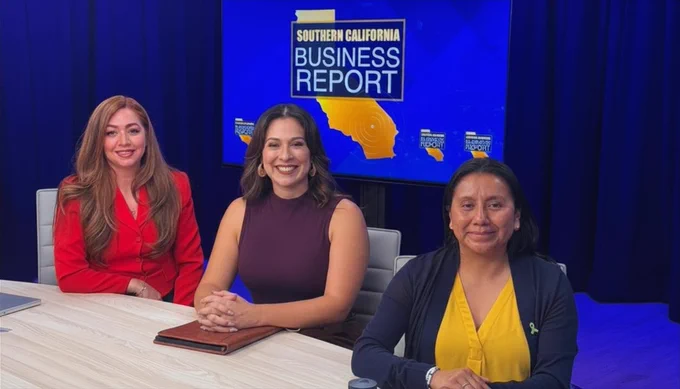 Three individuals are seated at a table on a TV set for "Southern California Business Report." A blue backdrop displays the show's logo.