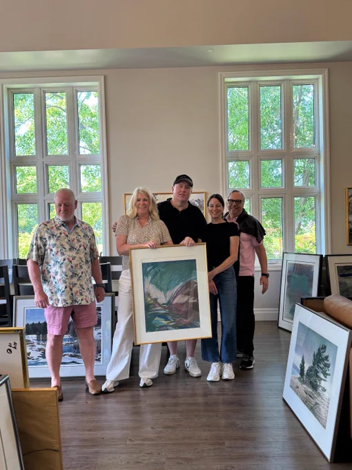 The ArtWorks for Cancer installation team working at Stedman Community Hospice poses in a bright room with tall windows, amidst the beautiful artworks to be installed.