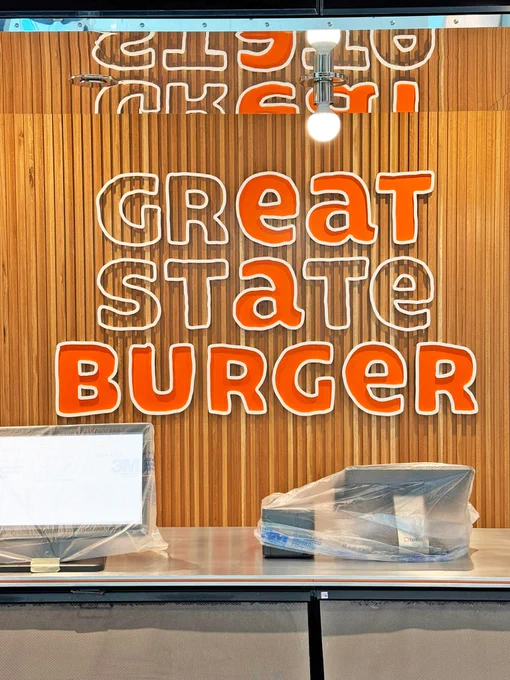 Restaurant counter with \"GREAT STATE BURGER\" sign on a wooden slatted wall.