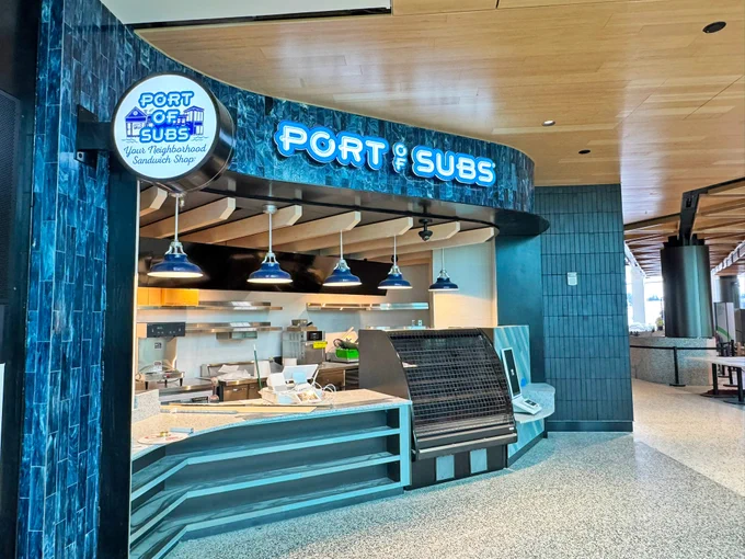 Exterior of a \"Port of Subs\" sandwich shop with blue sign and pendant lights.