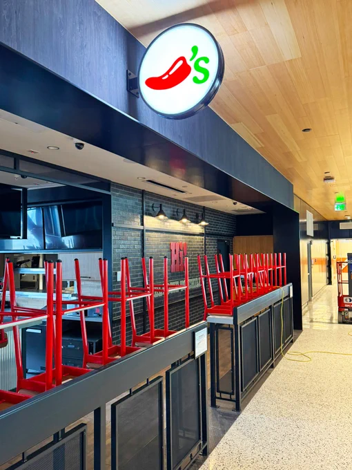 Restaurant exterior with a sign showing a chili pepper and 'S', and upside-down red stools on counters.