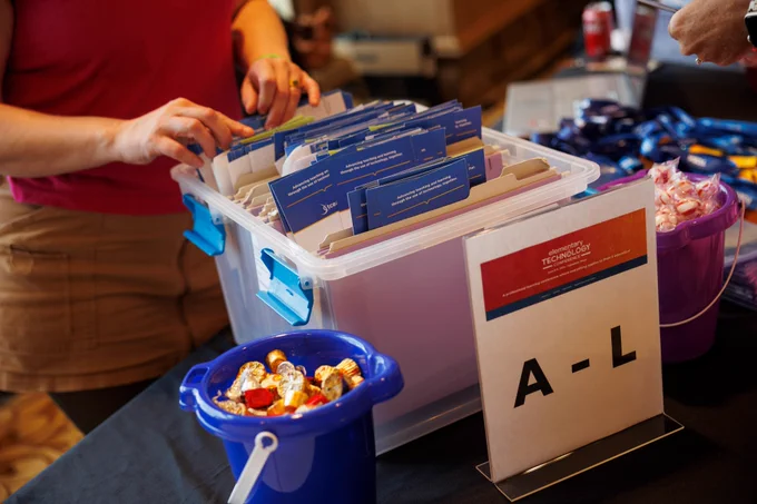 Photo of a person tending to a box full of folders. There is a sign in front of the box showing "A - L," indicating the folders are for attendees with last names A-L.