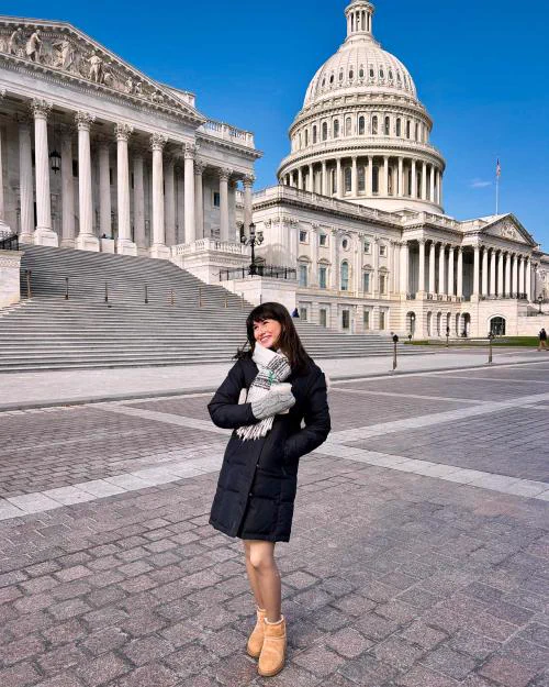 Person posing in a winter coat, on a paved plaza in view of the U.S. Capitol Building