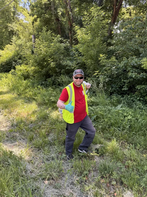 Hydrite volunteer wearing reflective vest holds up a high-five in a wooded area.