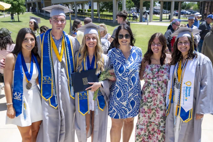 Four Rose State College graduates smile for a photo in their caps and gowns after graduation with their PLC group.