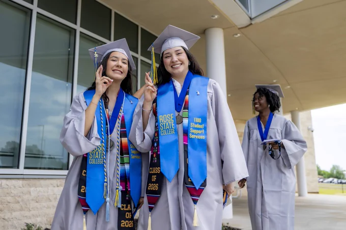 Two Rose State College graduates smile for a photo in their caps and gowns before graduation.