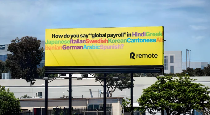 Remote payroll software billboard in San Francisco with yellow background displaying multilingual message asking "How do you say global payroll in Hindi, Greek, Portuguese, Japanese, Italian, Swedish, Korean, Cantonese, Albanian, German, Arabic, Spanish?"