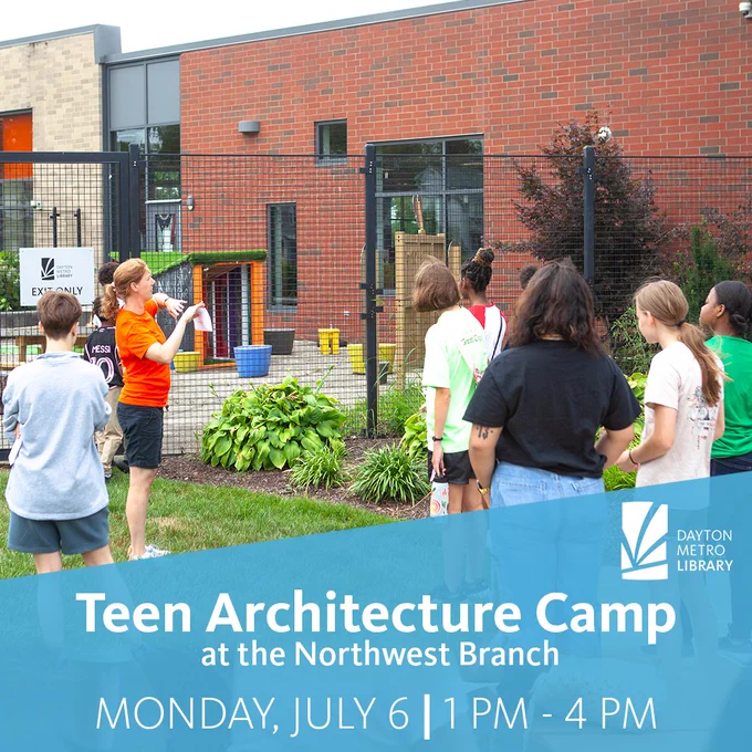 A group of teens stands outside near a fenced area beside a brick library building. An instructor gestures toward the space while the group listens, with plants and landscaping visible in the foreground.